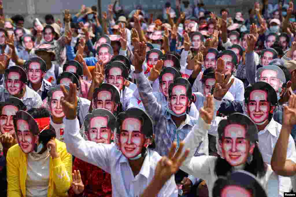 Protesters wearing masks depicting detained leader Aung San Suu Kyi, flash three-finger salutes as they take part in a protest against the military coup in Yangon, Myanmar, Feb. 28, 2021.