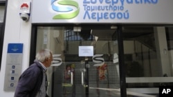 An elderly man holds his bank passbook as he looks through the windows of a closed cooperative bank shop in Limassol, Cyprus, Mar. 16, 2013.