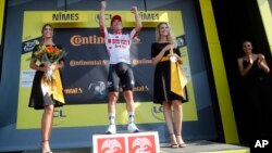L'Australien Caleb Ewan célèbrant sa victoire sur le podium, flanqué de deux hôtesses, après la seizième étape du Tour de France à Nîmes, le 23 juillet 2019. La pratique sexiste des "miss" sur le podium a finalement été modifiée en août 2020. (AP/Christophe Ena).
