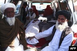 FILE - Afghan men sit next to the bodies of two students who were killed by a Taliban mortar round in a school, in the city of Ghazni, March 30, 2019.