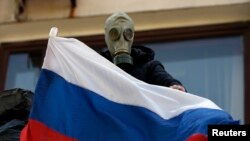 A pro-Russia rebel wearing a gas mask places a Russian flag on the balcony of the city hall in Mariupol, eastern Ukraine May 7, 2014. 