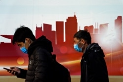 People wearing face masks to help curb the spread of the coronavirus walk by a mural depicting China's skyscrapers along a street in Beijing, Dec. 6, 2020.