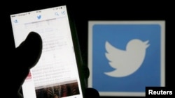 A man reads tweets on his phone in front of a displayed Twitter logo in Bordeaux, southwestern France, March 10, 2016.