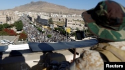 A Houthi militant sits guard on the roof of a building overlooking fellow Houthis rallying to denounce the rapid devaluation of the Yemeni Rial in Sanaa, Yemen, Oct. 5, 2018.