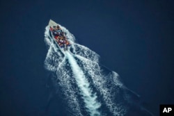 FILE - Migrants navigate on an overcrowded wooden boat in the Central Mediterranean Sea between North Africa and the Italian island of Lampedusa, Oct. 2, 2021, as seen from aboard the humanitarian aircraft Seabird.
