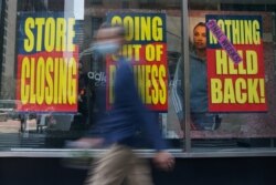 FILE - People walk past a business that is closing following the outbreak of COVID-19 in the Manhattan borough, New York, Aug. 17, 2020.