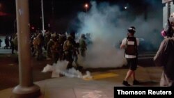 A member of the media stands amid tear gas used by police officers to clear protesters near an Immigration and Customs Enforcement centre in Portland 20 Aug 2020.