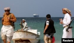 Armed men stand on the beach as the Galaxy Leader commercial ship, seized by Yemen's Houthis last month, is anchored off the coast of al-Salif on December 5, 2023. (Khaled Abdullah/Reuters)