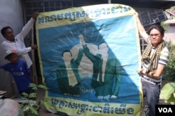 Cambodia National Rescue Party activists, Khan Lai, left, and Chham Sophan, right, held up a CNRP poster in Poipet, Banteay Meanchey province. (Sun Narin/VOA Khmer)