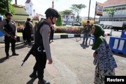 Seorang polisi menanyai seorang ibu di depan gerbang lokasi pemboman pada Senin, di Surabaya, Indonesia, 15 Mei 2018.