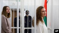 Jurnalis Katsiaryna Andreyeva (kanan) dan Daria Chultsova berdiri di balik sel tahanan di ruang pengadilan di Minsk, Belarus, Kamis, 18 Februari 2021. 