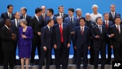 President Donald Trump, front center, listens to France's President Emmanuel Macron as they pose with world leaders for a group picture at the start of the G20 Leader's Summit inside the Costa Salguero Center in Buenos Aires, Argentina, Friday, Nov. 30, 2018.