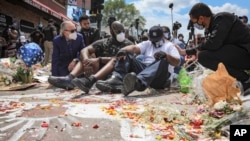 FILE - in this June 1, 2020 file photo, an emotional Terrence Floyd, second from right, is comforted as he sits at the spot at the intersection of 38th Street and Chicago Avenue, Minneapolis, Minn., where his brother George Floyd, encountered police.