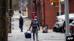 រូបឯកសារ៖ ស្រ្តីម្នាក់ពាក់ម៉ាសដើរអូសរទេះដាក់ឥវ៉ាន់ឆ្លងផ្លូវមួយនៅក្រុងញូវយ៉ក សហរដ្ឋអាមេរិក កាលពីថ្ងៃទី៣០ ខែមីនា ឆ្នាំ២០១៩។