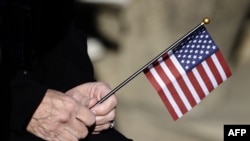 FILE - A woman holds a miniature US flag during a Veterans Day ceremony at Arlington National Cemetery in Arlington, Virginia.