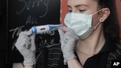 Harmons grocery store employee Samantha Kapptie holds a free digital thermometer at their pharmacy drive-thru window, April 1, 2020, in Salt Lake City. 