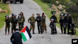 FILE - A demonstrator holds a Palestinian flag in front of Israeli forces as Palestinians protest against President Donald Trump's Mideast initiative, in Jordan Valley in the West Bank, Feb. 25, 2020. 