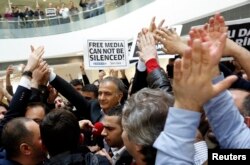 FILE - Zaman editor-in-chief Ekrem Dumanli, escorted by plainclothes police officers, is cheered on by his colleagues as he leaves the headquarters of Zaman daily newspaper in Istanbul, Dec. 14, 2014. Turkish police had raided media outlets close to U.S.-based Muslim cleric Fethullah Gulen and detained 23 people nationwide in operations against what President Tayyip Erdogan said was a network conspiring to topple him.