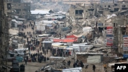 ผู้คนเดินผ่านแผงขายของท่ามกลางซากปรักหักพังของอาคารที่ถูกทำลายระหว่างการโจมตีของอิสราเอลครั้งก่อน ในเมืองข่าน ยูนิส ทางตอนใต้ของฉนวนกาซาเมื่อวันที่ 15 มกราคม 2025 ในขณะที่สงครามในดินแดนปาเลสไตน์ระหว่างอิสราเอลและฮามาสยังคงดำเนินต่อไป (AFP)