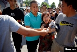 A woman is detained by security personnel outside the U.S. embassy in Beijing, China, July 26, 2018.