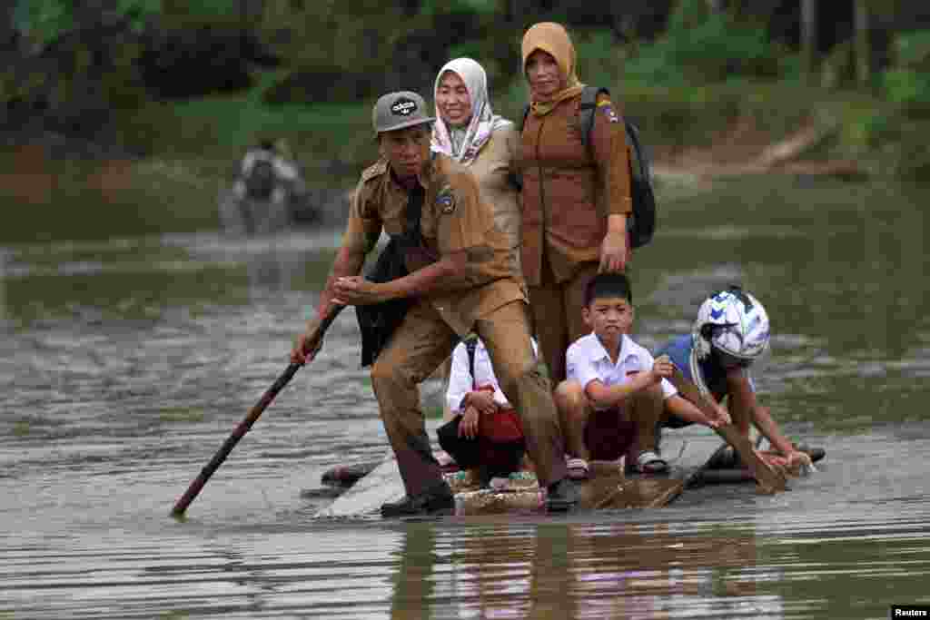 A group of teachers and some oftheir students use a makeshift raft as they cross the flooded street in Ranomeeto Barat village in Konawe Selatan, Sulawesi island, Indonesia.