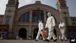 FILE - In this April 7, 2020, file photo, workers in protective suits walk past the Hankou railway station on the eve of its resuming outbound traffic in Wuhan in central China's Hubei province. 