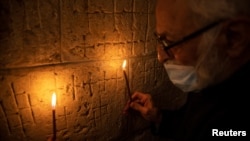 Father Samuel Aghoyan, the Armenian superior at the Church of the Holy Sepulchre, holds candles to illuminate crosses etched into the ancient stone wall of the Saint Helena chapel inside the church. (REUTERS/Ronen Zvulun)