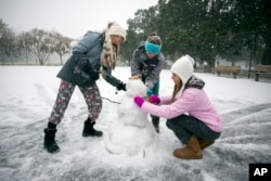 Children from the Hoffman and Lynns families build a snowman on the public basketball courts in Forsyth Park, Jan. 3, 2018, in Savannah, Georgia.
