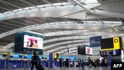 Travellers wearing face coverings walk with their luggage in the almost deserted departures hall at Terminal 5 of Heathrow Airport in west London on Dec. 21, 2020.