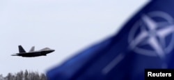 FILE - NATO flag flutters as U.S. Air Force F-22 Raptor fighter flies over the military air base in Siauliai, Lithuania, April 27, 2016.
