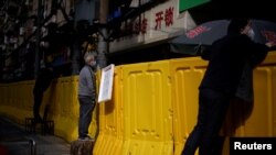 Residents wearing face masks pay for groceries by standing on chairs to peer over barriers set up to ring fence a wet market on a street in Wuhan, Hubei province, the epicenter of China's coronavirus disease (COVID-19) outbreak, April 1, 2020. 