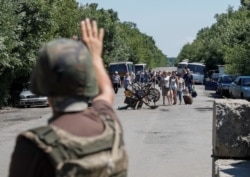 FILE - A member of the Ukrainian State Border Guard Service signals for people to stop as they approach a checkpoint at the contact line between Russia-backed rebels and Ukrainian troops, in Mayorsk, eastern Ukraine, July 3, 2019.