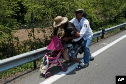 A Central American migrant pushing a child in a baby carriage is detained by a Mexican immigration agent from behind on the highway to Pijijiapan, Mexico, April 22, 2019.