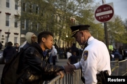 FILE - Ninth-grader Tremaine Holmes shakes hands with Captain Erik Pecha in front of the Baltimore Police Department Western District station in Baltimore, April 23, 2015.
