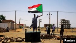 Seorang pengunjuk rasa Sudan mengibarkan bendera sambil berdiiri di atas barikade di sebuah jalan Khartoum, Sudan, 5 Juni 2019.