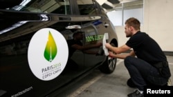 FILE - An employee installs a sticker which reads 100% electric next to the logo of the upcoming COP21 Climate Change Conference on a Nissan LEAF electric car in Boulogne-Billancourt, near Paris, France, November 16, 2015.