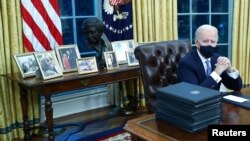 Biden family photos are displayed around a bust of activist Cesar Chavez, as U.S. President Joe Biden prepares to sign executive orders at the Resolute Desk inside the Oval Office of the White House in Washington, U.S., January 20, 2021. Picture taken Jan