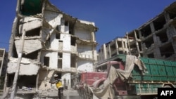 Seorang anggota Pertahanan Sipil Suriah, yg dikenal sebagai Helm Putih, berdiri di depan bangunan yang rusak berat akibat serangan udara oleh pasukan rezim di kota Idlib, 12 Juli 2019. (Foto: dok)