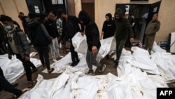 Petugas medis dan sukarelawan menyiapkan jenazah yang tewas dalam serangan Israel semalaman di kamp pengungsi Al-Maghazi, menjelang pemakaman massal di rumah sakit Al-Aqsa di Deir Al-Balah, di Jalur Gaza selatan, pada 25 Desember 2023. (Foto: AFP)