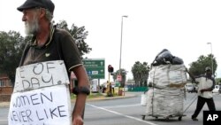 FILE - A man, left, begs, as another collects recyclable materials, at a street intersection in Johannesburg, South Africa, March 16, 2016.