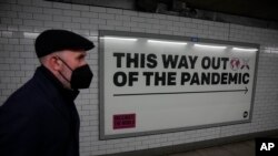 Seorang pria mengenakan masker saat berjalan melewati sebuah papan pengumuman kampanye kesehatan di underpass yang menuju stasiun kereta bawah tanah Westminster di London, pada 27 Januari 2022. (Foto: AP/Matt Dunham) 