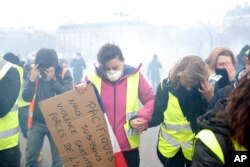 FILE - "Yellow vest" protesters run away from tear gas during clashes with riot police, in Paris, France, Jan. 12, 2019.
