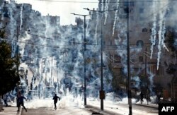 Palestinian stone throwers run to take cover after Israeli security forces fired tear gas canisters during clashes following a demonstration next to the Israeli controversial separation wall in the West Bank city of Bethlehem, Dec. 18, 2015.