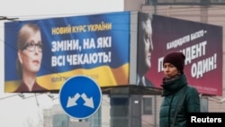FILE - A woman stands in front of pre-election posters of opposition politician Yulia Tymoshenko and Ukrainian President Petro Poroshenko in Kyiv, Ukraine, Feb. 20, 2019. 