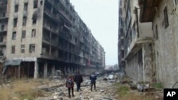 This frame grab from Dec. 13, 2016 video, shows people walking among damaged buildings on a street filled with debris near the ancient Umayyad Mosque, in the Old City of Aleppo, Syria. 