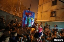 FILE - A woman holds a child as they get ready to hit a pinata at a birthday party celebration in Caracas, Venezuela, April 13, 2019.