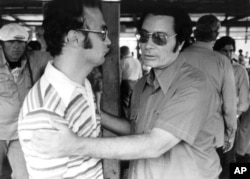 Rev. Jimmy Jones, founder of People's Temple, clasps an unidentified man at Jonestown, Nov. 18, 1978, during Congressman' Leo J. Ryan's visit.