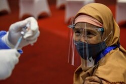 Seorang perempuan yang memakai masker dan pelindung wajah terlihat saat petugas kesehatan bersiap untuk menyuntiknya dengan vaksin Sinovac selama program vaksinasi massal COVID-19 di Bursa Efek Indonesia di Jakarta, 31 Maret 2021. (Foto: REUTERS/Willy Kur