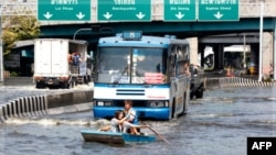 Cư dân chèo thuyền phía trước một xe buýt dọc theo con đường bị ngập lụt ở Bangkok, ngày 7/11/2011