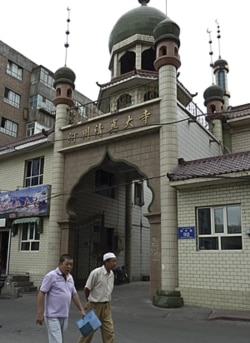 FILE - Members of the Uyghur ethnic minority walk past a mosque near the Erduoqiao neighborhood in Urumqi in northwestern China's Xinjiang Uyghur Autonomous Region.